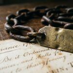 Close-up of an 18th-century Gunter’s surveying chain with brass marker resting on a handwritten 1785 land survey map