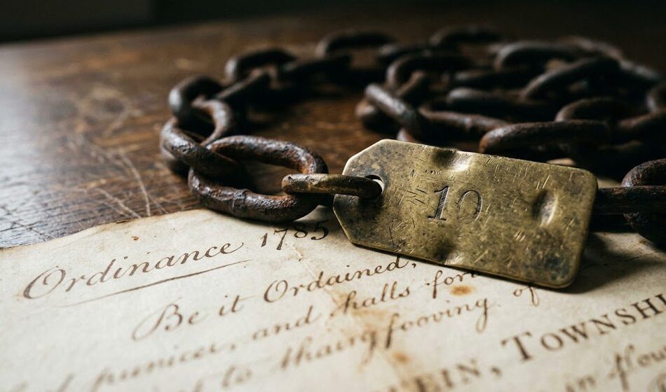 Close-up of an 18th-century Gunter’s surveying chain with brass marker resting on a handwritten 1785 land survey map