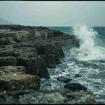 Raw documentary photograph of an ancient Roman harbor breakwater resisting violent storm waves, demonstrating durable coastal engineering.