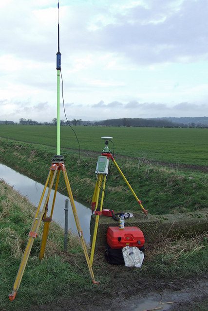 A surveyor operating an RTK GPS rover unit mounted on a pole in a field