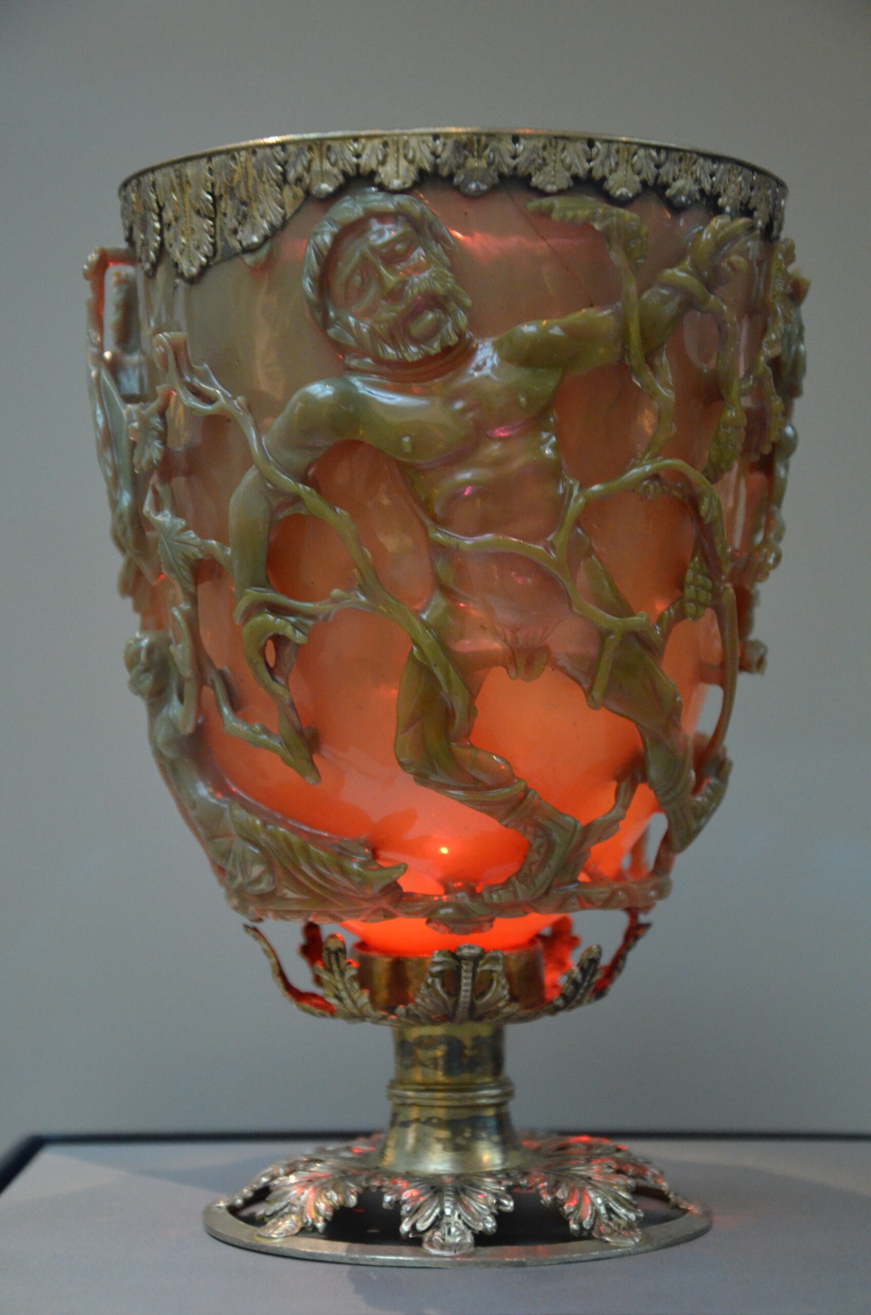 The Roman Lycurgus Cup glowing translucent red due to backlighting, highlighting the detailed cage carving.