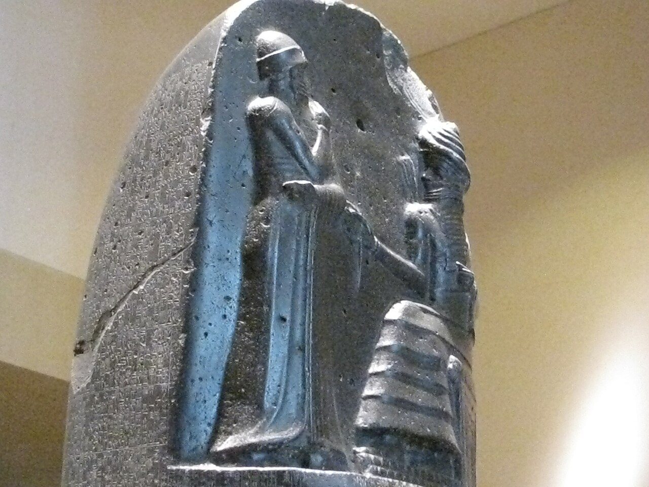 Tall black diorite stele inscribed with cuneiform law code, topped with a relief of a king before a seated god