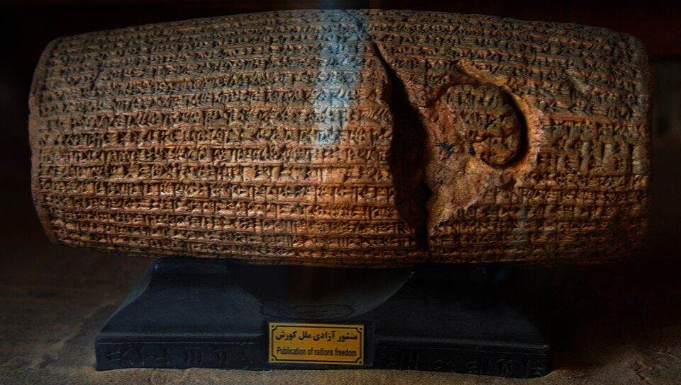 Barrel-shaped clay cylinder covered in Akkadian cuneiform inscriptions