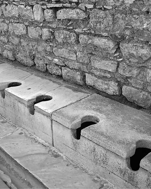 Row of stone public toilets with keyhole openings in Ephesus.
