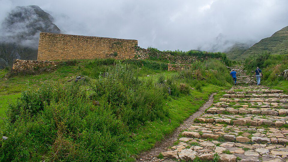 Stone-paved Inca road crossing a green Andean mountain landscape near an ancient settlement
