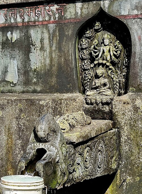Ornate stone water spout in a sunken brick basin.