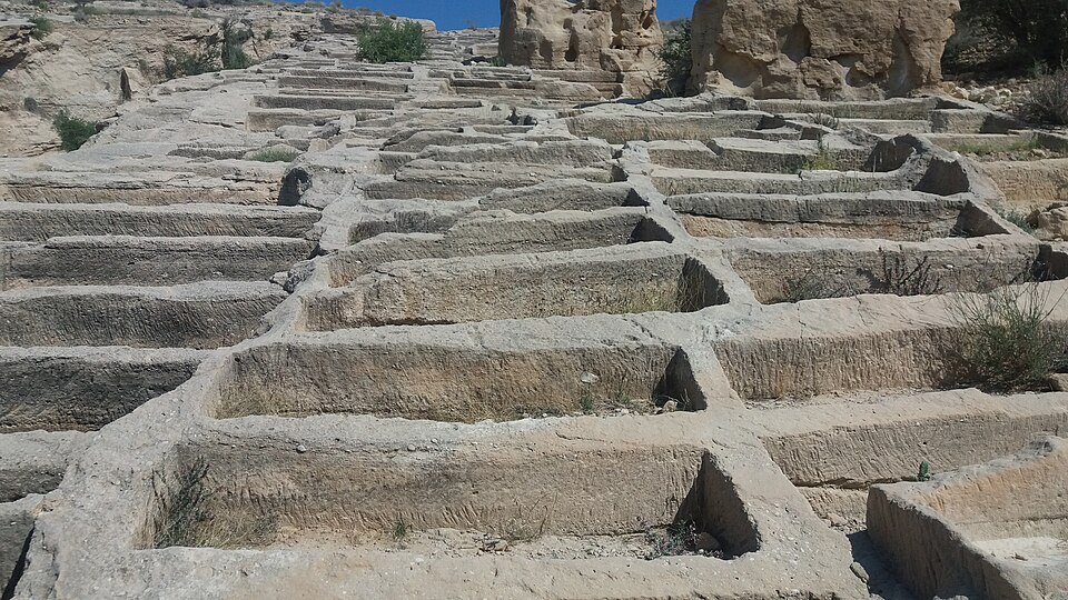 Deep vertical shafts and stone remnants at the Siraf archaeological site.