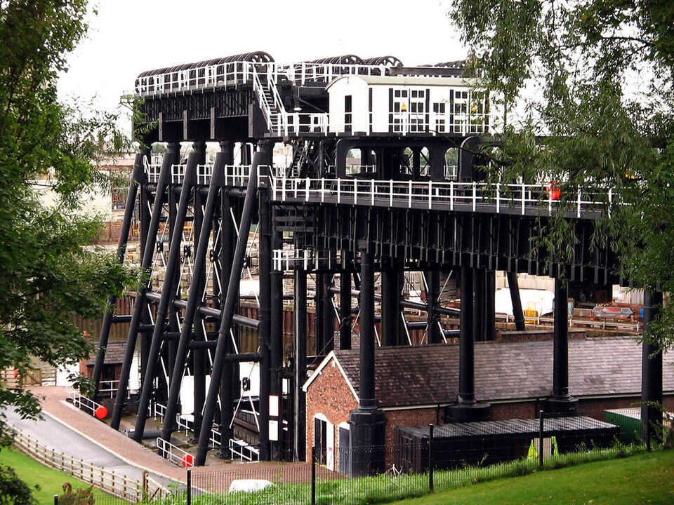 A towering black iron framework holding massive water tanks over a river.