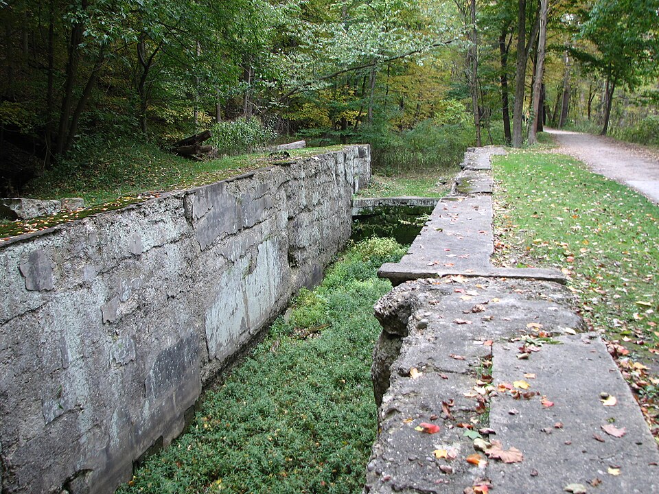 Dry-laid sandstone blocks forming a crumbling canal lock in a wooded park.